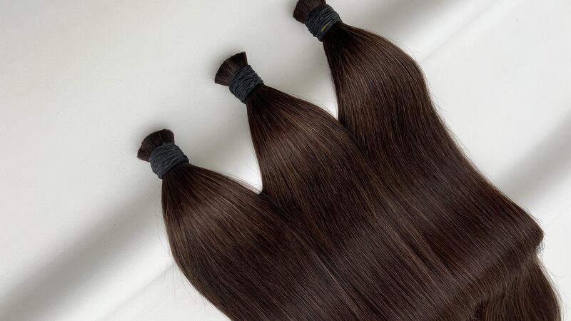Bundles of straight bulk human hair in colour #4 Chocolate Brown laid on a plain background, with the bound ends towards the front.