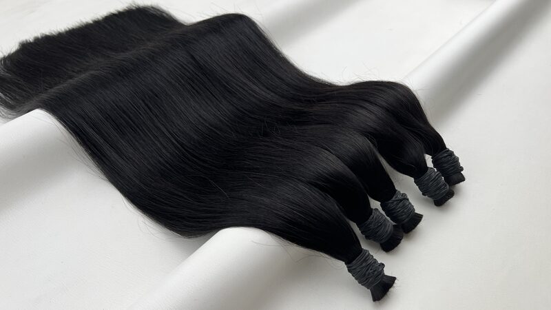 Bundles of straight bulk human hair in colour #1B Natural Black on a plain background, the ends tied at the base.